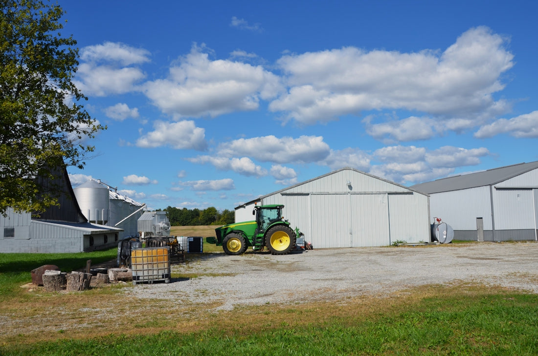 Green tractor parked near farm buildings under blue sky.